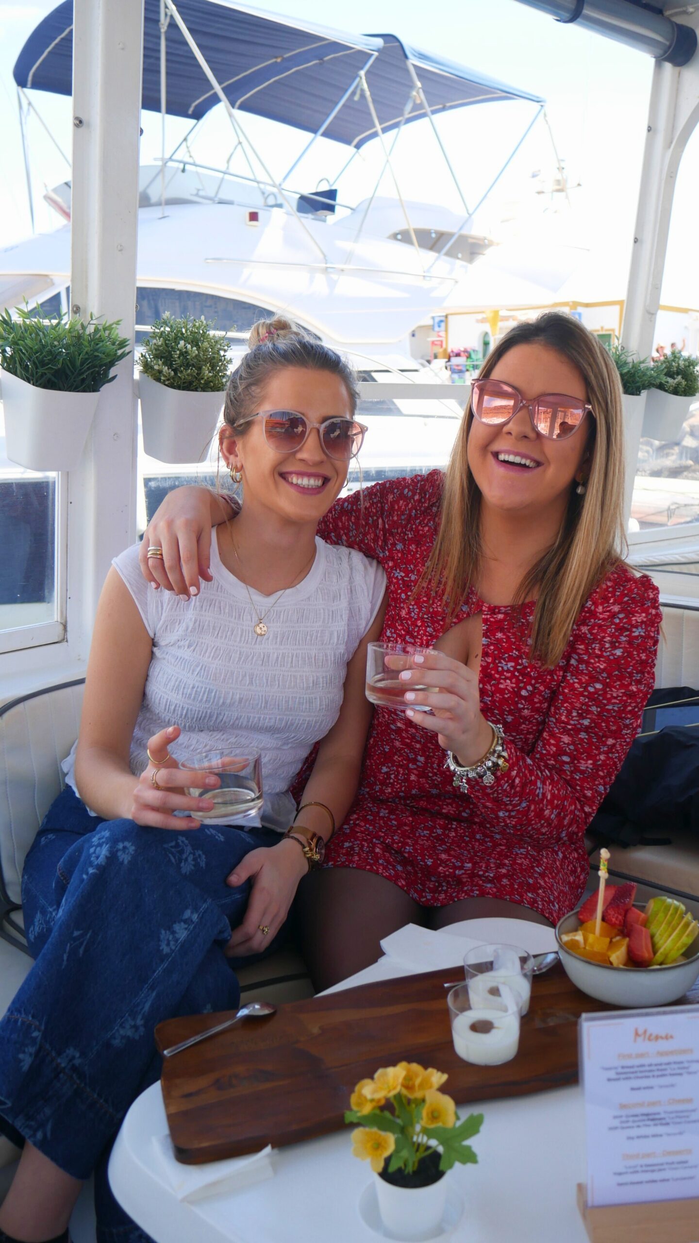 Friends Enjoying a Tasting Experience on Board – Yellow Boat Mogan Two smiling women enjoying a drink and fruit tasting on board Yellow Boat Mogan, docked at the marina in Puerto de Mogán, Gran Canaria.